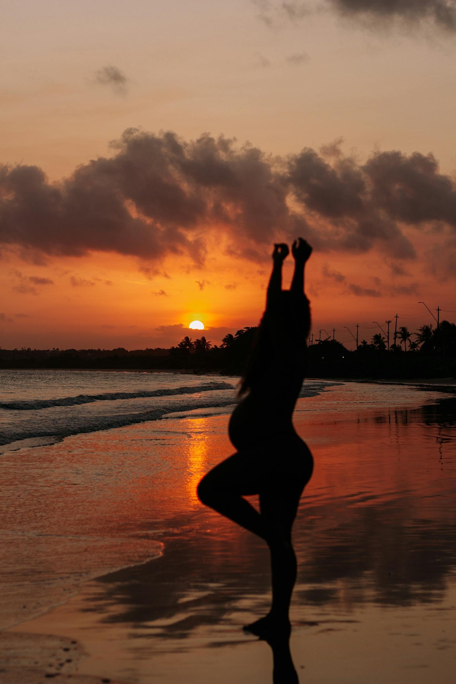 Silhouette of a pregnant woman doing yoga on a serene beach at sunset, exuding tranquility and anticipation.